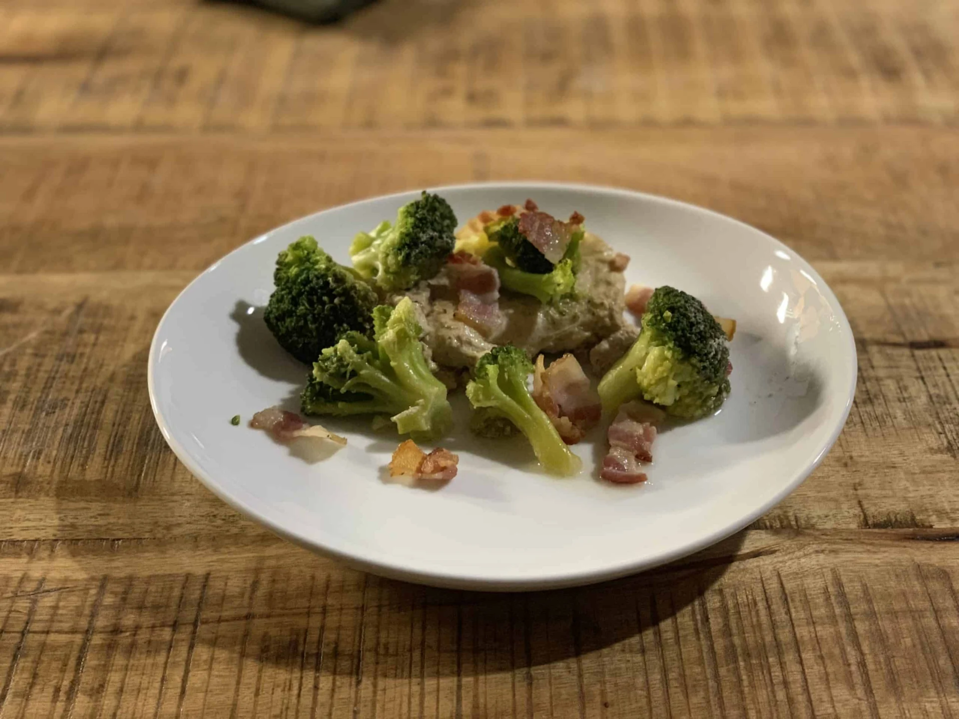 A plate of broccoli and bacon on a wooden table.