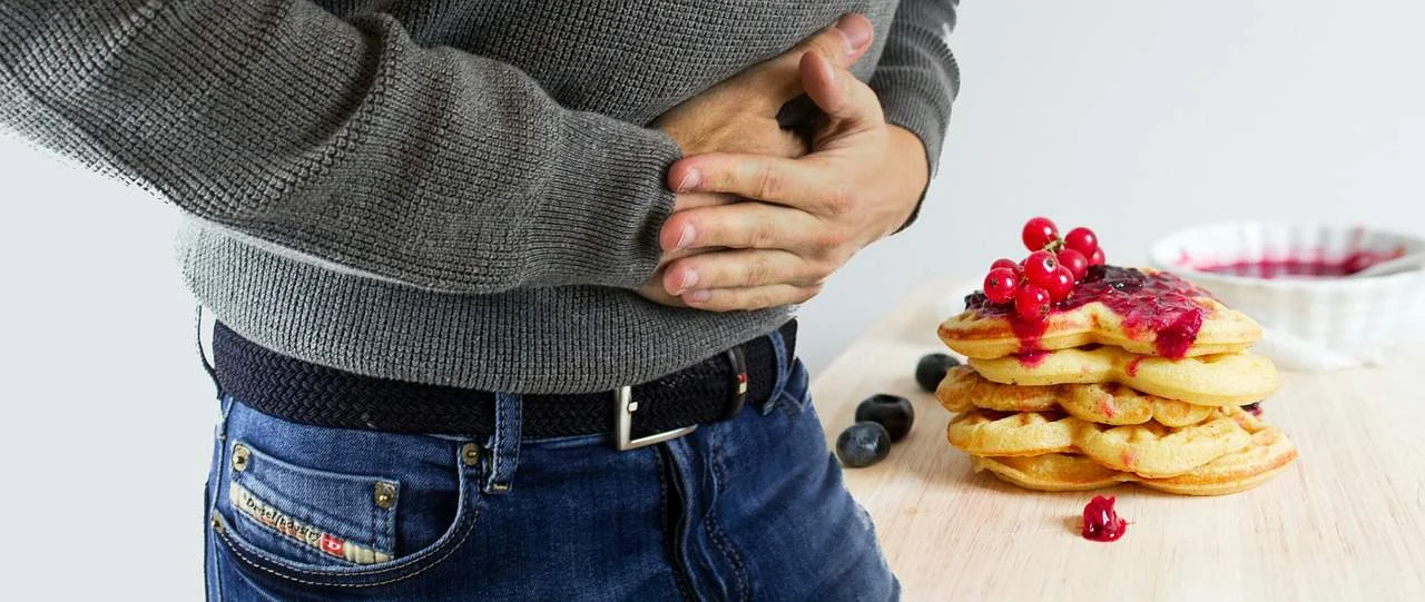 A man with a stomachache holding a plate of pancakes.